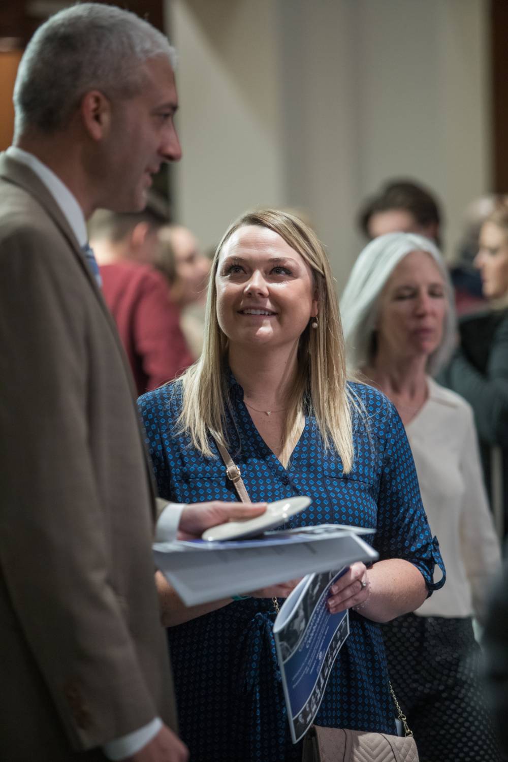 Woman smiling and listening to a man. Both have Fall 2019 Graduate Student Celebration programs in their hands